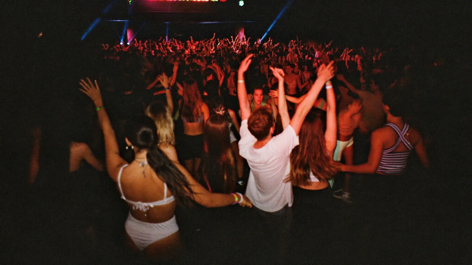 A crowd dancing under coloured lights on a party boat deck