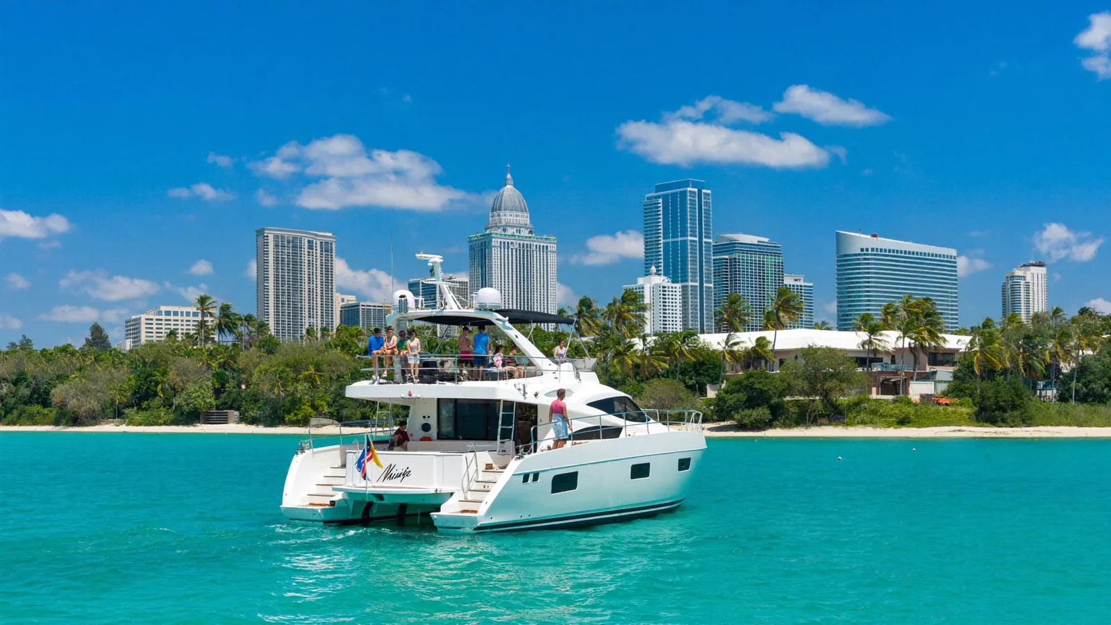 A white catamaran on turquoise water with the Miami skyline and palm trees behind