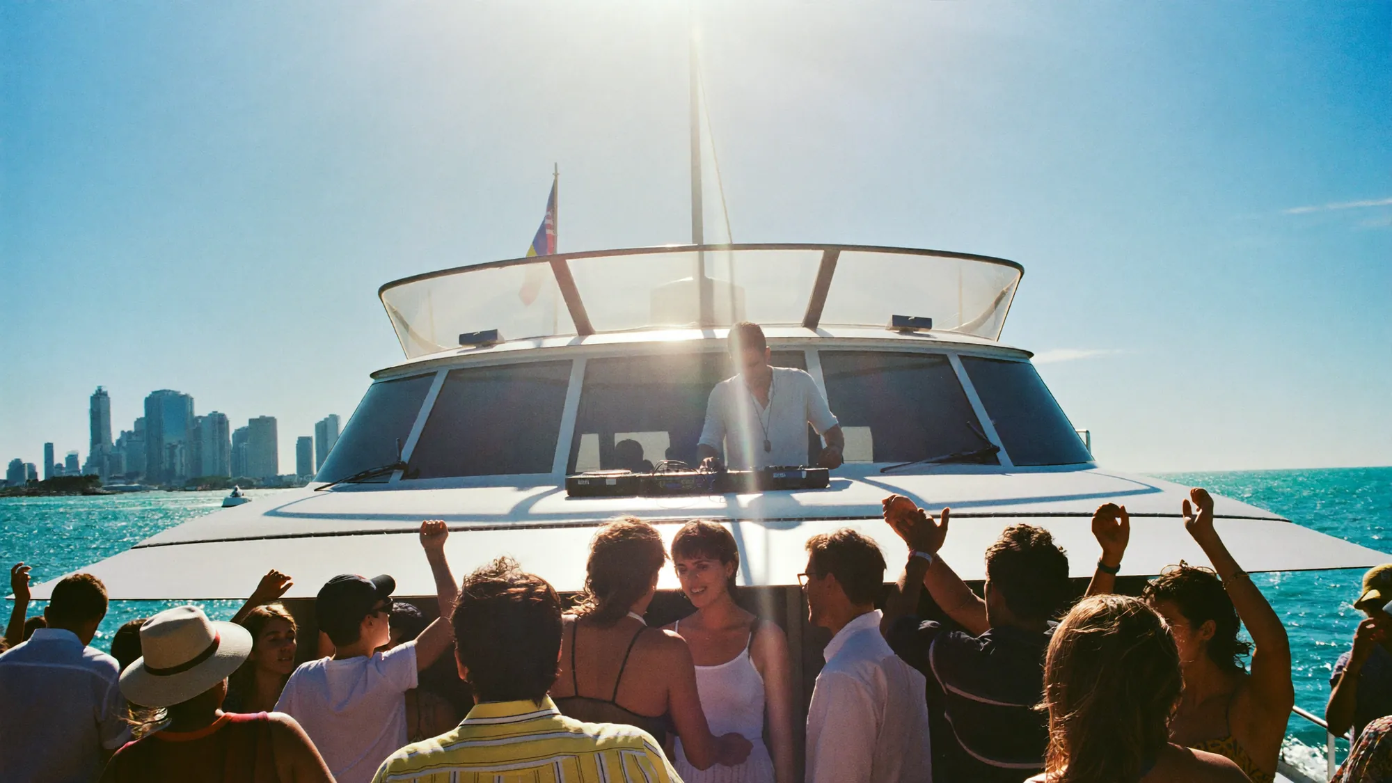 A crowd dancing to a DJ on the deck of a party boat in bright sunshine