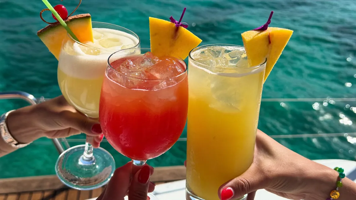 Colourful tropical cocktails raised in a toast over turquoise water