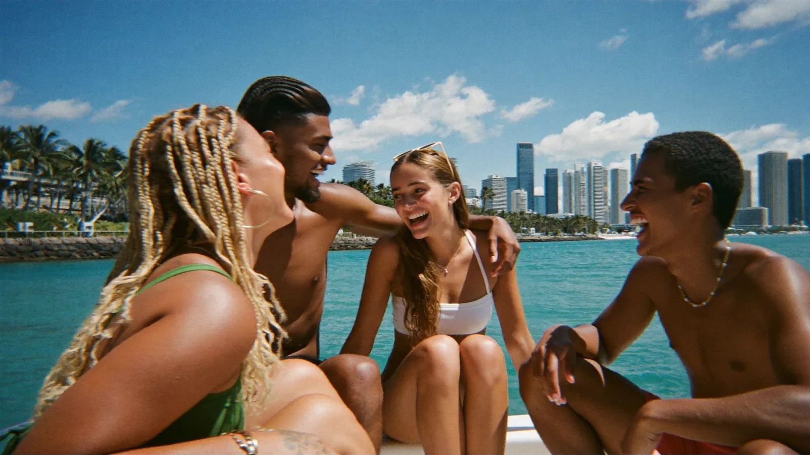 Friends laughing together on the bow of a boat, turquoise water and the Miami skyline behind them
