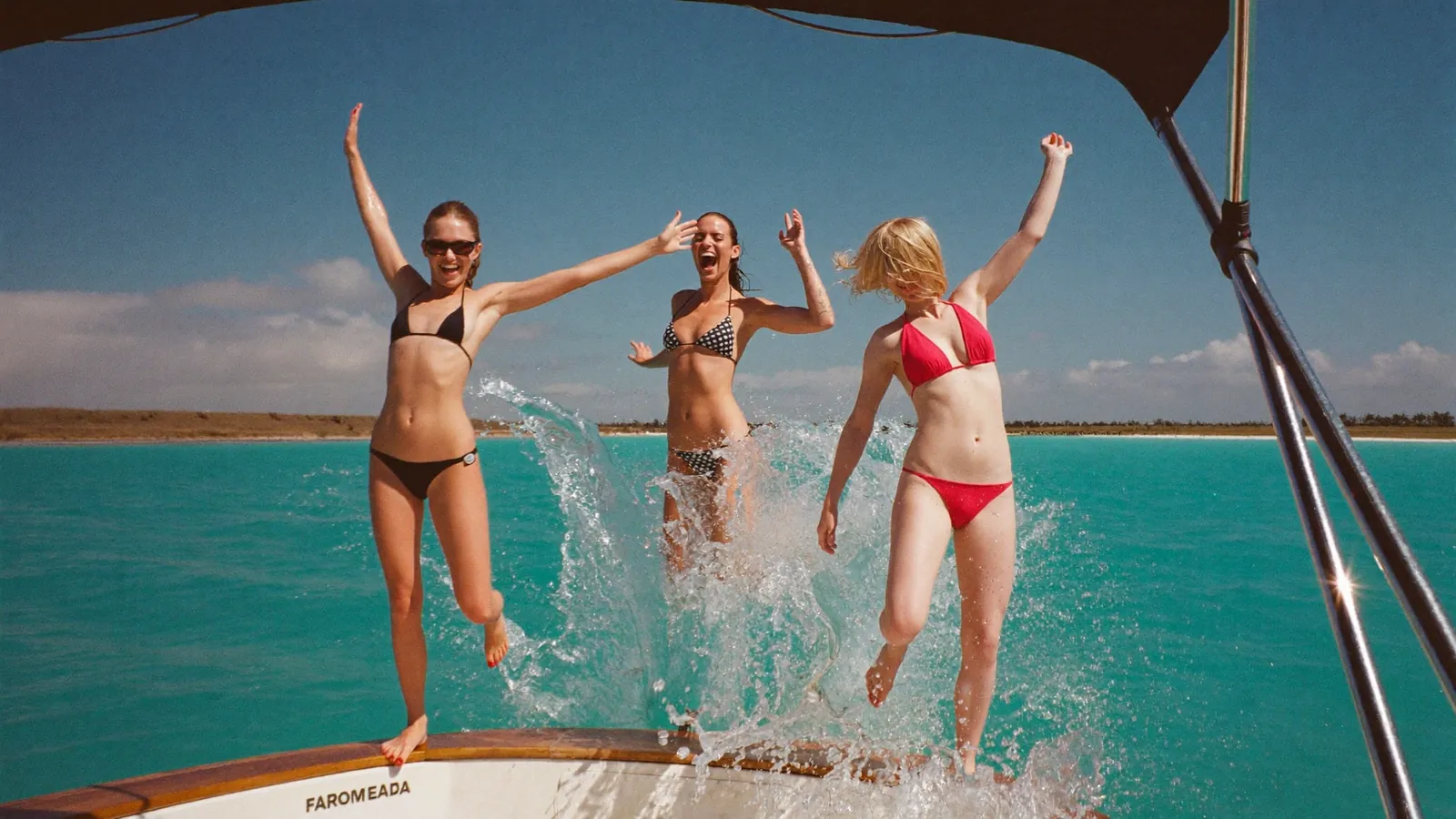 Three friends jumping off the back of a boat into turquoise water